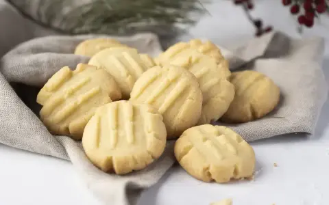 Montón de galletas de mantequilla doradas con líneas marcadas, servidas sobre una tela gris.