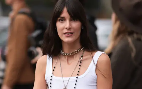 Frau mit langen Haaren und Curtain Bangs, trägt weiße Tanktop und Chanel-Schmuck.