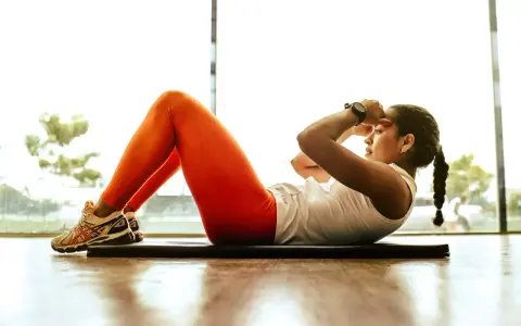 Kobieta w pomarańczowych legginsach ćwiczy brzuszki. Efekty ćwiczeń widoczne są jako redukcja cellulitu.
