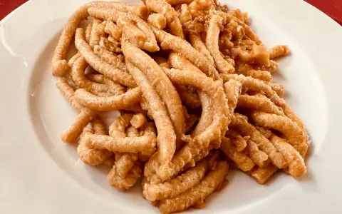 Pici all'aglione, uno dei piatti tipici di Arezzo, serviti su un piatto bianco.