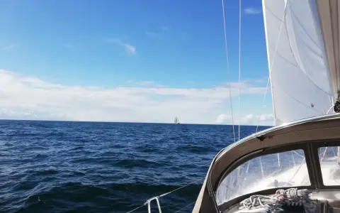 Segeln in Deutschland: Ein Segelboot gleitet über das Meer, im Hintergrund ein weiterer Segler unter blauem Himmel.