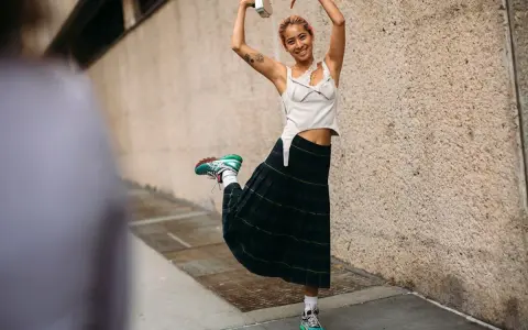 Joven sonriente con falda escocesa y top blanco, luciendo unos modernos looks con zapatillas deportivas.