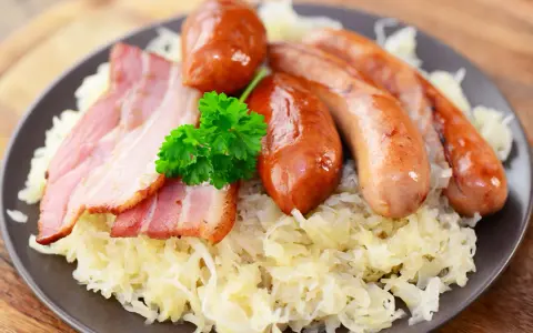 Assiette de choucroute allemande ou alsacienne garnie de saucisses et de lardons, décorée d'une touche de persil frais.