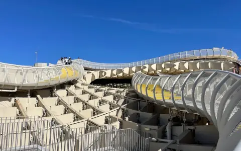 The Metropol Parasol, known as Las Setas de Sevilla, features a modern wooden structure with winding walkways and yellow steps under a clear blue sky.