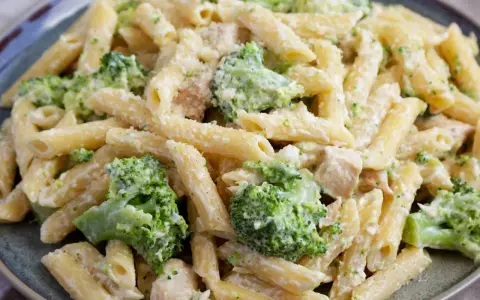 Penne z kurczakiem i brokułami w kremowym sosie, posypane parmezanem. Pyszny makaron z brokułami na talerzu.