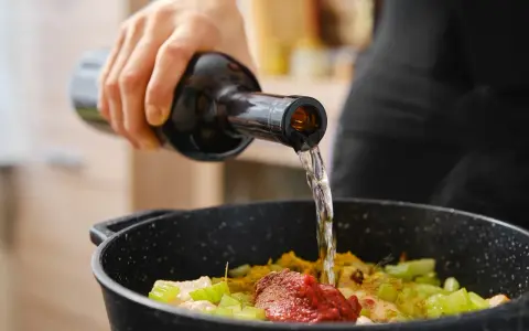 Una mano vierte vino en una sartén con ingredientes. El vino en moderación realza el sabor de la comida.