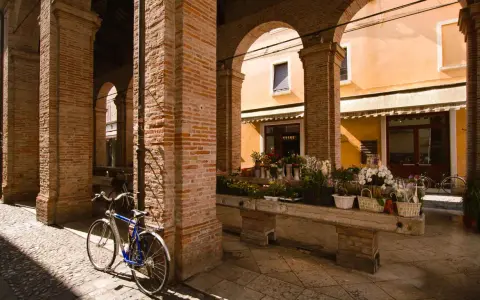 Sotto gli archi di mattoni rossi, un tempo la vecchia pescheria, ora un fiorista espone i suoi colori. Una bicicletta blu riposa sul selciato.