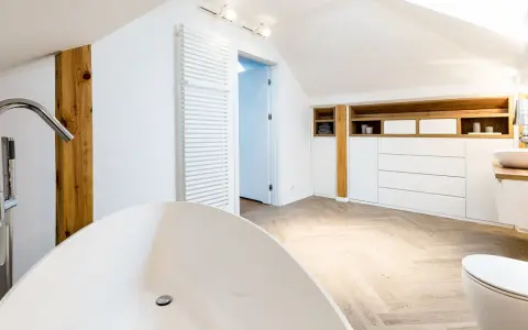Élégante salle de bain sous pente avec baignoire îlot, lavabo, toilettes et rangements en bois.