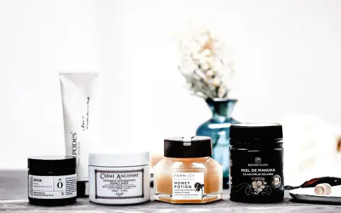 Plusieurs masques pour le visage, dont un masque au miel, sont disposés sur une table en bois.
