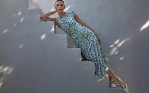 A woman in a floral dress and white heels, embodying a chic formal dress code for women, poses on white stairs.