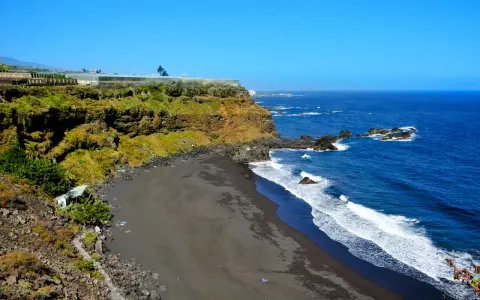 Spiaggia di sabbia nera e scogliere verdi sulle isole delle Canarie, con il blu intenso dell'oceano Atlantico.