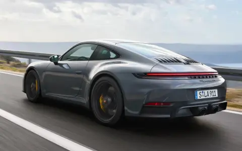 Grauer Porsche 911 Hybrid rast auf einer Küstenstraße.