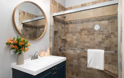 Salle de bain moderne avec douche carrelée, lavabo et miroir rond. Idéal pour nettoyer VMC et profiter d'un espace sain.