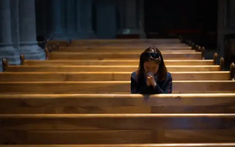 Kobieta w kościele, z rękami złożonymi do modlitwy, szuka nadziei w sprawach beznadziejnych.