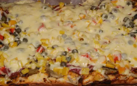 Pyszna pizza na grubym cieście z warzywami i roztopionym serem.