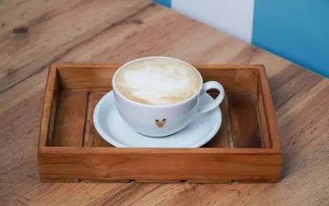 Eine Tasse Kaffee au lait mit Herz-Detail auf einem Holzteller, bereit zum Genießen.