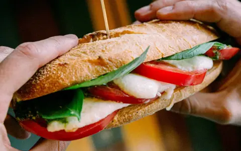 Ręce trzymają pyszne włoskie pieczywo z mozzarellą, pomidorami i bazylią. Idealne na szybki lunch.