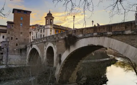 El puente Fabricio, con sus arcos de piedra y la torre medieval, cruza el Tíber bajo un cielo anaranjado.
