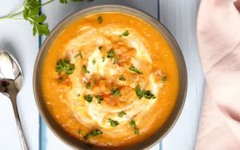 Un bol de soupe crémeuse aux lentilles corail, garni de crème et de persil frais, prêt à être dégusté avec une cuillère.