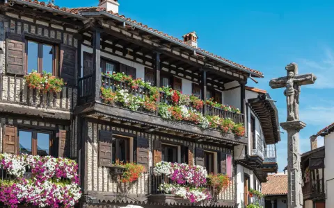 Casas de madera y piedra adornadas con flores en la Sierra de Francia. Un crucero de piedra se alza en la plaza.