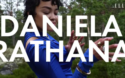 Daniela Rathana i blå klänning i skogen, med texten "DANIELA RATHANA" över bilden. Hon bär smycken och hennes pappa är troligen stolt.