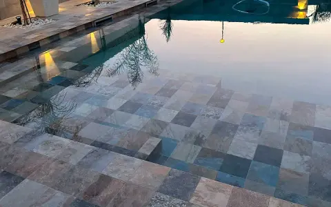 Escalones de piscina con diversos tipos de gresite para piscinas, creando un mosaico de tonos grises, azules y marrones.