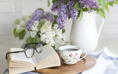 Un libro aperto, occhiali, tazza di caffè e fiori di lillà. Un'atmosfera rilassante, perfetta per pensare a come eliminare gli odori in casa.