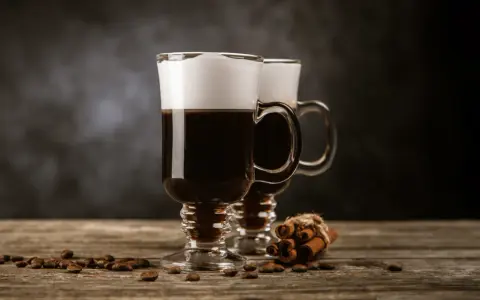 Två glas med kaffe och grädde, kaffebönor och kanelstänger på ett träbord. Perfekt för ostbollar till drinken.