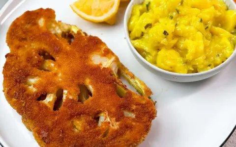 Knuspriges Blumenkohl-Schnitzel mit Kartoffelsalat und Zitronenspalten auf einem Teller.