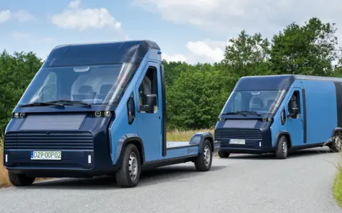Dwa nowoczesne, niebieskie polskie samochody elektryczne na drodze wśród zieleni. Jeden to podwozie, drugi to furgonetka.
