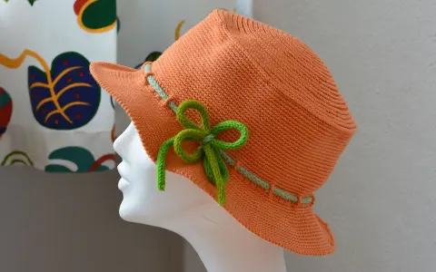 En orange virkad hatt med ljusgröna detaljer och en rosett. Perfekt för sommaren!