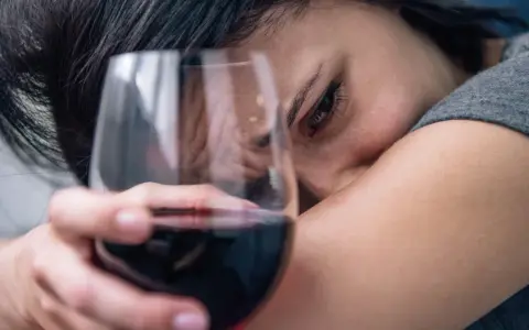 Smutna kobieta z kieliszkiem wina, jakby słuchała piosenki o alkoholu.