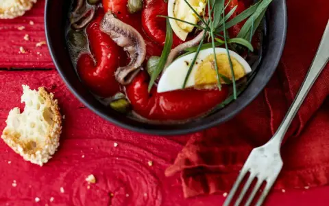 Salade de poivrons grillés avec anchois, câpres, œuf dur et herbes fraîches, servie avec du pain grillé.