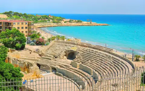 Ancient Roman amphitheater ruins overlooking a beautiful beach and turquoise sea. Discover Tarragona things to do, from history to relaxation.