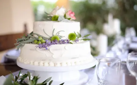 Dwupoziomowy tort weselny ozdobiony kwiatami, ziołami i oliwkami. Delikatne kremowe wykończenie i naturalne dekoracje podkreślają wyjątkowe smaki tortów weselnych.