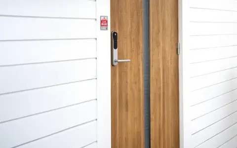 En modern ytterdörr med ett Verisure Yale Doorman V2N lås. Dörren är i trä och har en vitmålad panelvägg bredvid.
