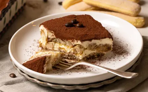 Ein Stück Tiramisu, perfekt für ein Tiramisu Rezept, mit Löffelbiskuit, Creme und Kakaopulver bestäubt.