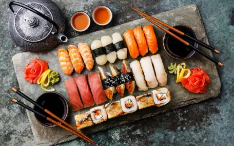 Piękny zestaw sushi: nigiri z łososiem, krewetkami, tuńczykiem i węgorzem, a także rolki. Obok czajniczek i filiżanki z herbatą. Idealne na co do sushi.