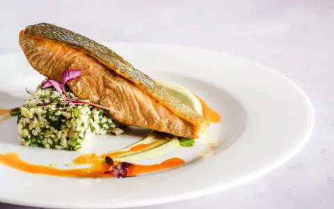 Wykwintna fotografia jedzenia: soczysty łosoś z chrupiącą skórką, podany na kaszy z ziołami i kremowym puree.
