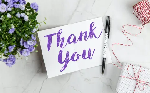 Carte "Thank You" violette, entourée de fleurs bleues, d'un stylo étoilé et d'un cadeau emballé. Une belle façon de remercier quelqu'un pour sa gentillesse.