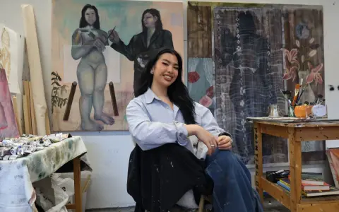 A young woman, one of many talented gen z artists, smiles in her studio, surrounded by her evocative paintings.
