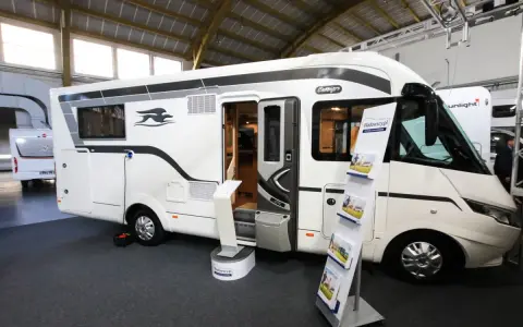 Biała kamperka z otwartymi drzwiami na targach caravaningowych Poznań. W środku widać wyposażenie, a na zewnątrz stojaki z ulotkami.