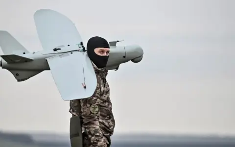 Mann in Tarnkleidung und schwarzer Sturmhaube trägt eine Drohne. Seit wann gibt es Drohnen? Die Geschichte reicht weit zurück.