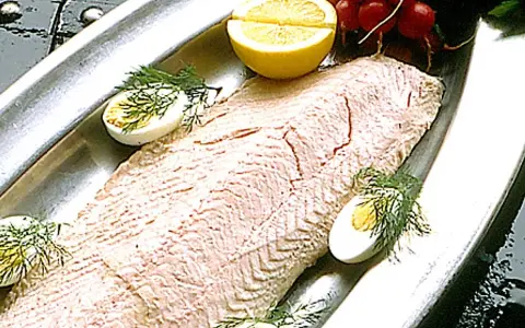 En vacker inkokt lax serveras på ett silverfat med citronklyftor, kokta ägg och dill.