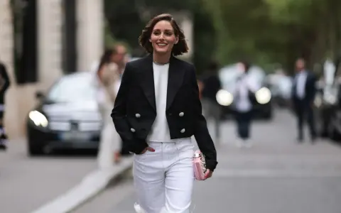 Mujer sonriente con chaqueta negra y pantalones blancos, lista para una comida familiar de invierno.