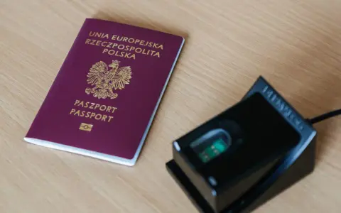 Polski paszport i czytnik linii papilarnych na drewnianym blacie.