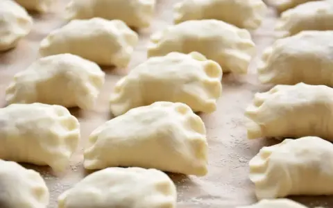 Gotowe do gotowania ciasto na pierogi, ułożone rzędami na blacie.