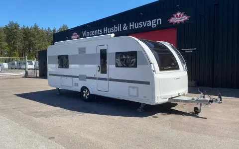 En vit Adria Alpina 613 UT husvagn står parkerad framför en byggnad med texten "Vincents Husbil & Husvagn".