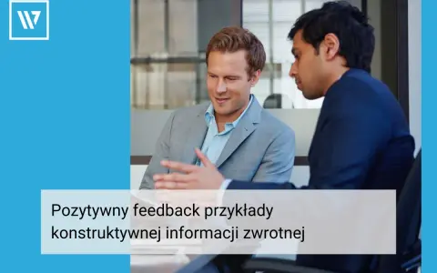Dwóch mężczyzn w garniturach rozmawia przy biurku. Jeden z nich gestykuluje, omawiając pozytywny feedback dla pracownika, przykłady konstruktywnej informacji zwrotnej.