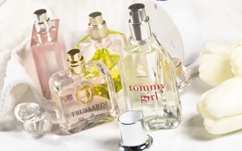 Mehrere Parfümflaschen, darunter Trussardi und Tommy Girl, auf weißem Handtuch mit weißen Tulpen.